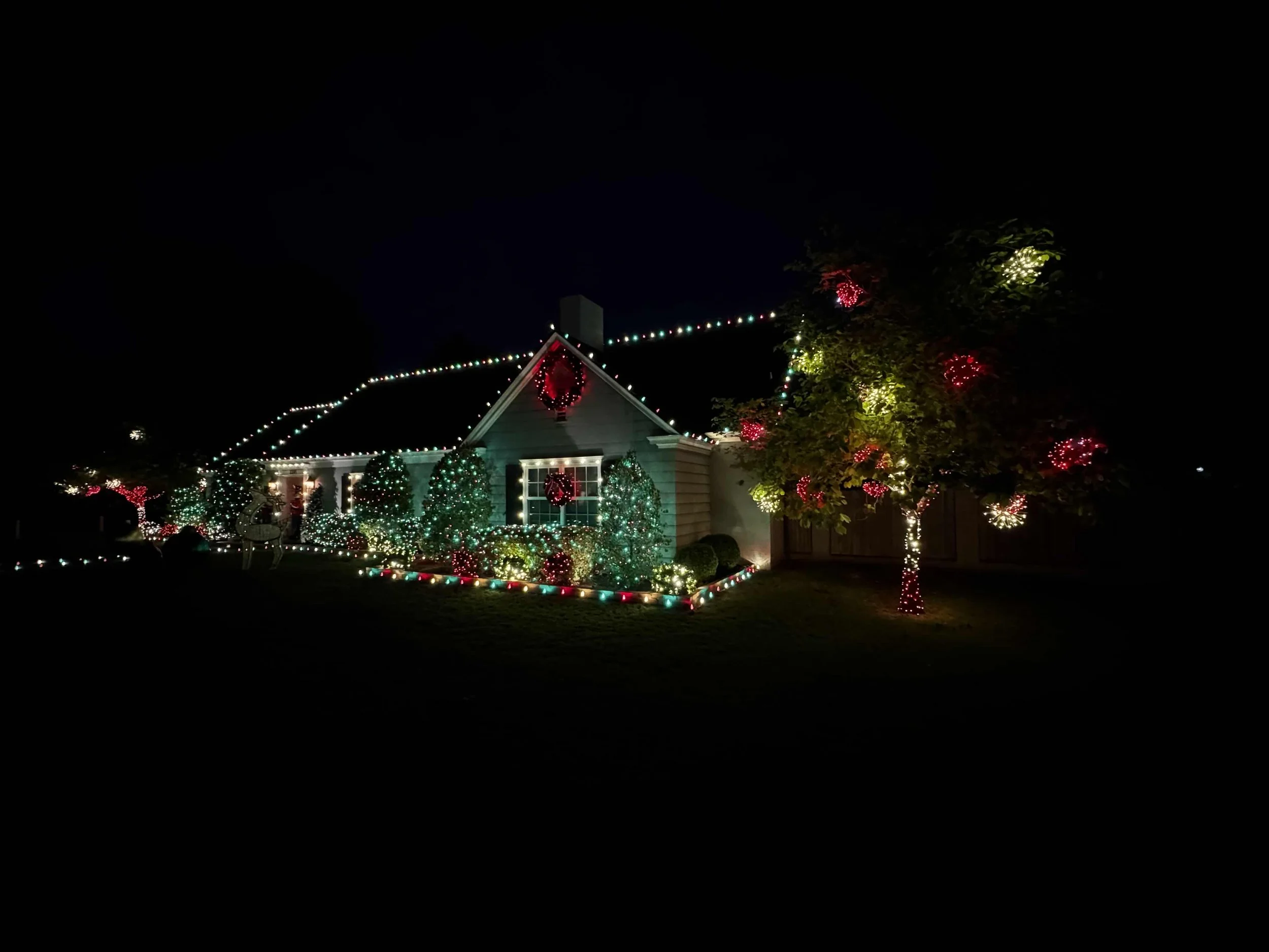 A house at night decorated with green, red, and gold multicolor string lights and a lit wreath above the front door. Orlando Christmas Lights, Winter Park Holiday Lighting, Windermere Christmas Light Installation Near Me
