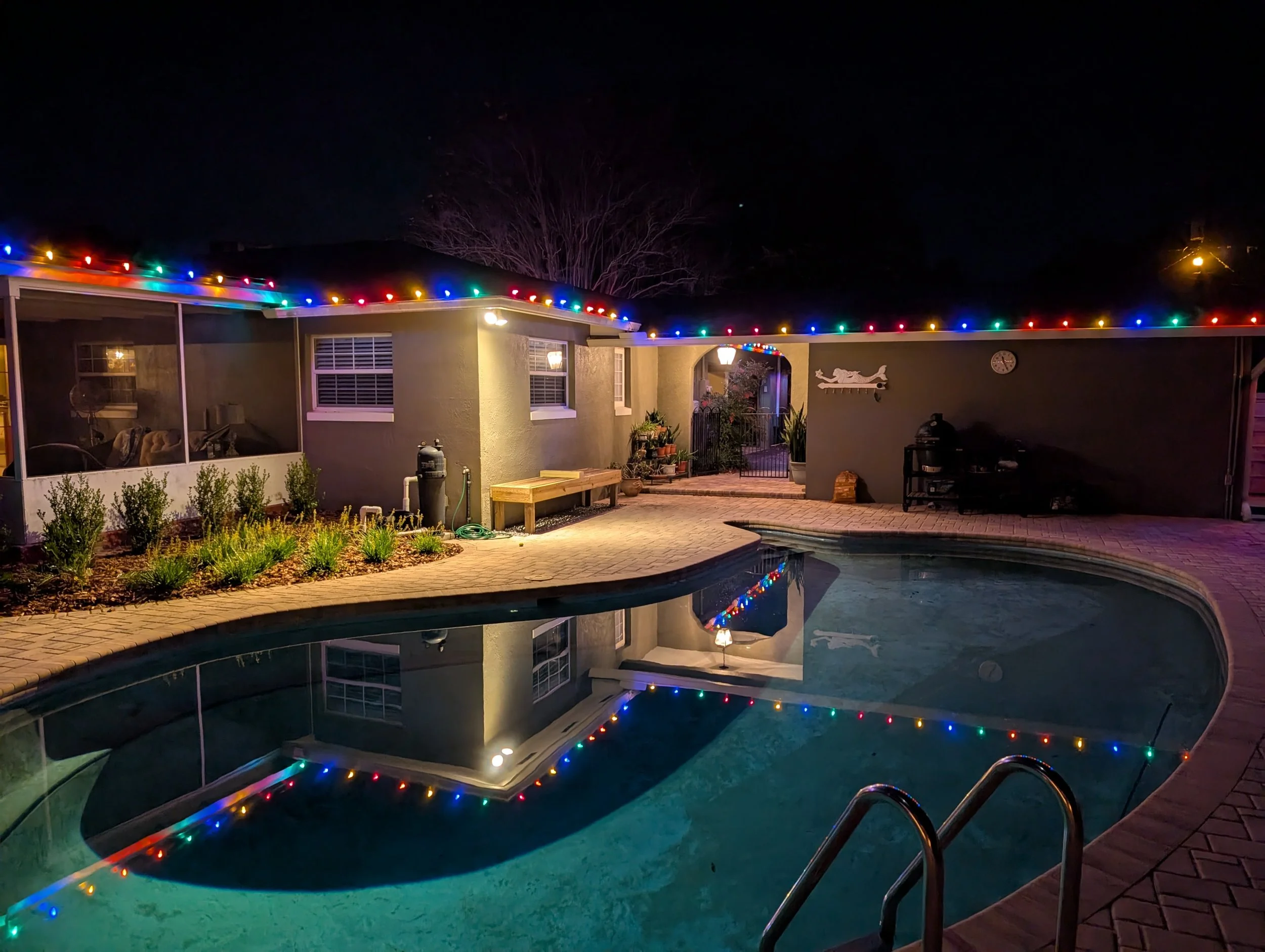 A backyard pool at night outlined with colorful string lights along the screened pool enclosure. Orlando Christmas Lights, Winter Park Holiday Lighting, Windermere Christmas Light Installation Near Me
