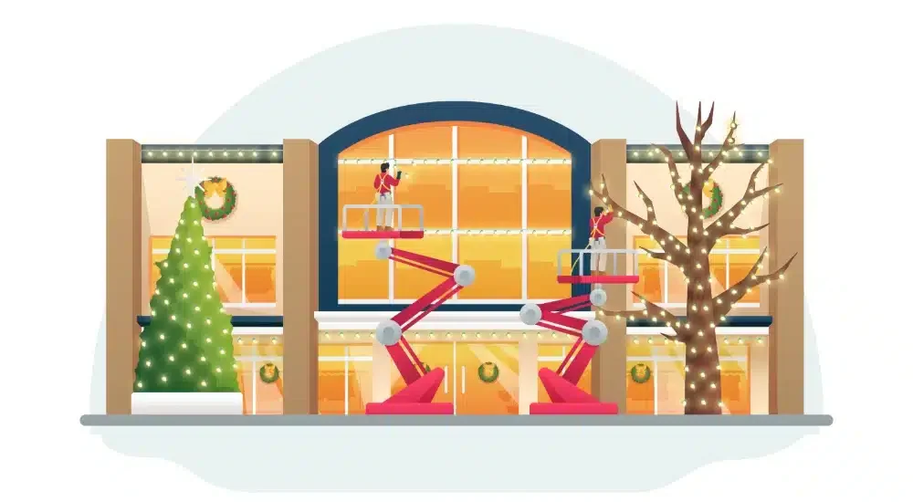 A holiday display with a large decorated Christmas tree with lights, a leafless tree wrapped in lights, and miniature toy soldiers on platforms, set on a building window with holiday wreaths.