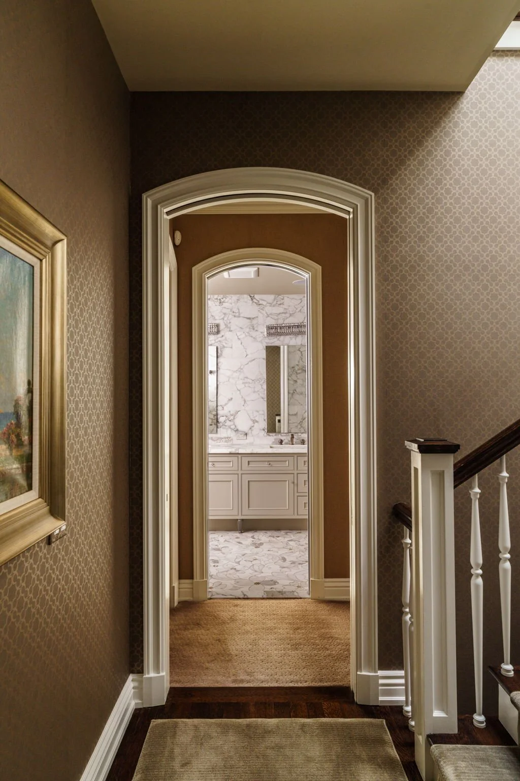 View down a hallway leading to a bathroom with marble walls and a white vanity.