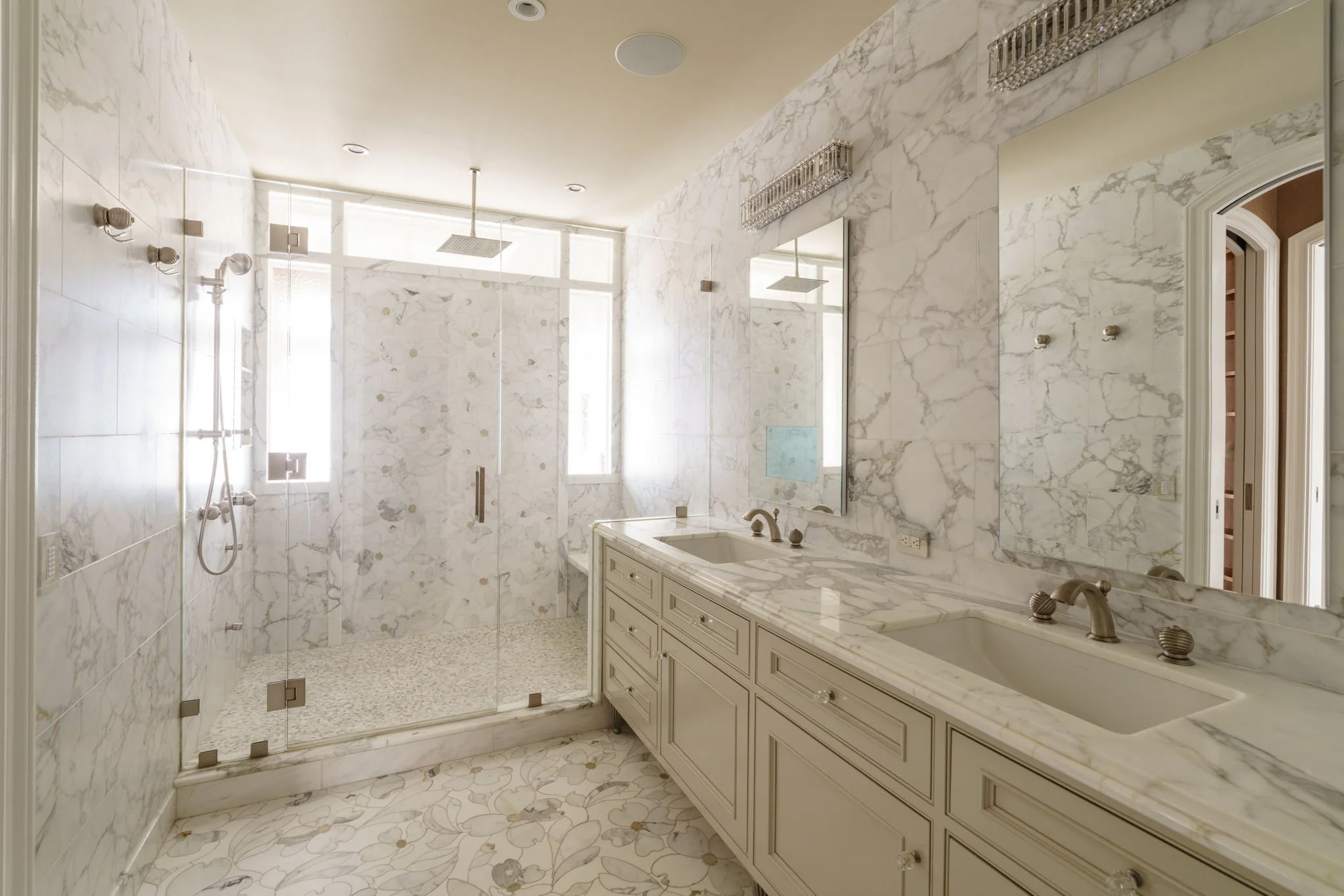 Bathroom with marble walls, a double sink vanity, and a glass-enclosed shower with rain showerhead.