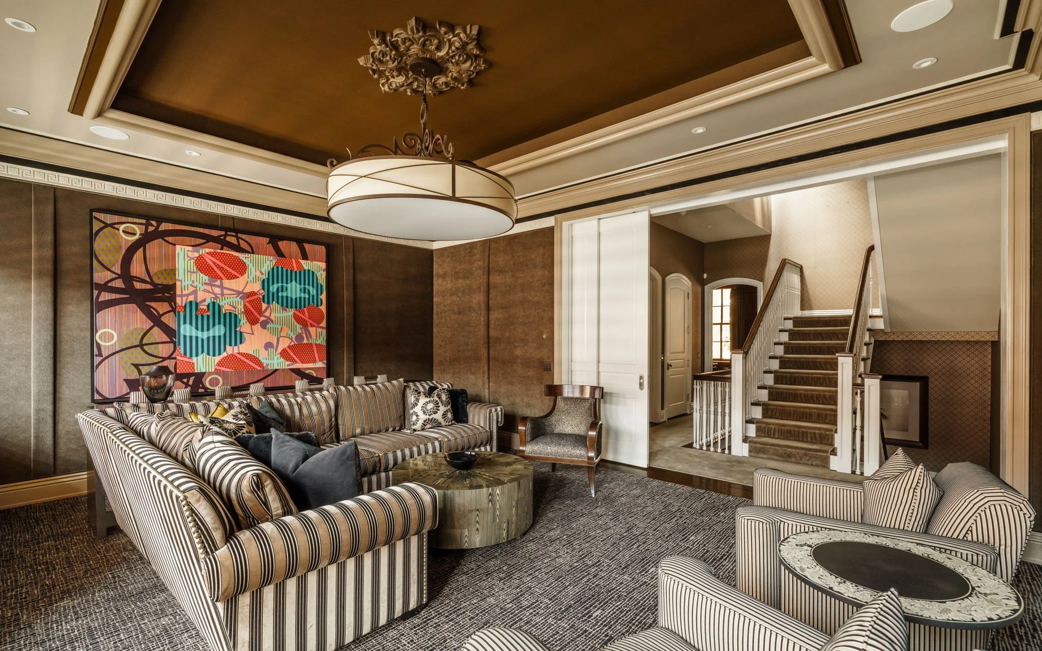 Living room with striped sofas, a striped armchair, colorful wall art, and a staircase leading upstairs.