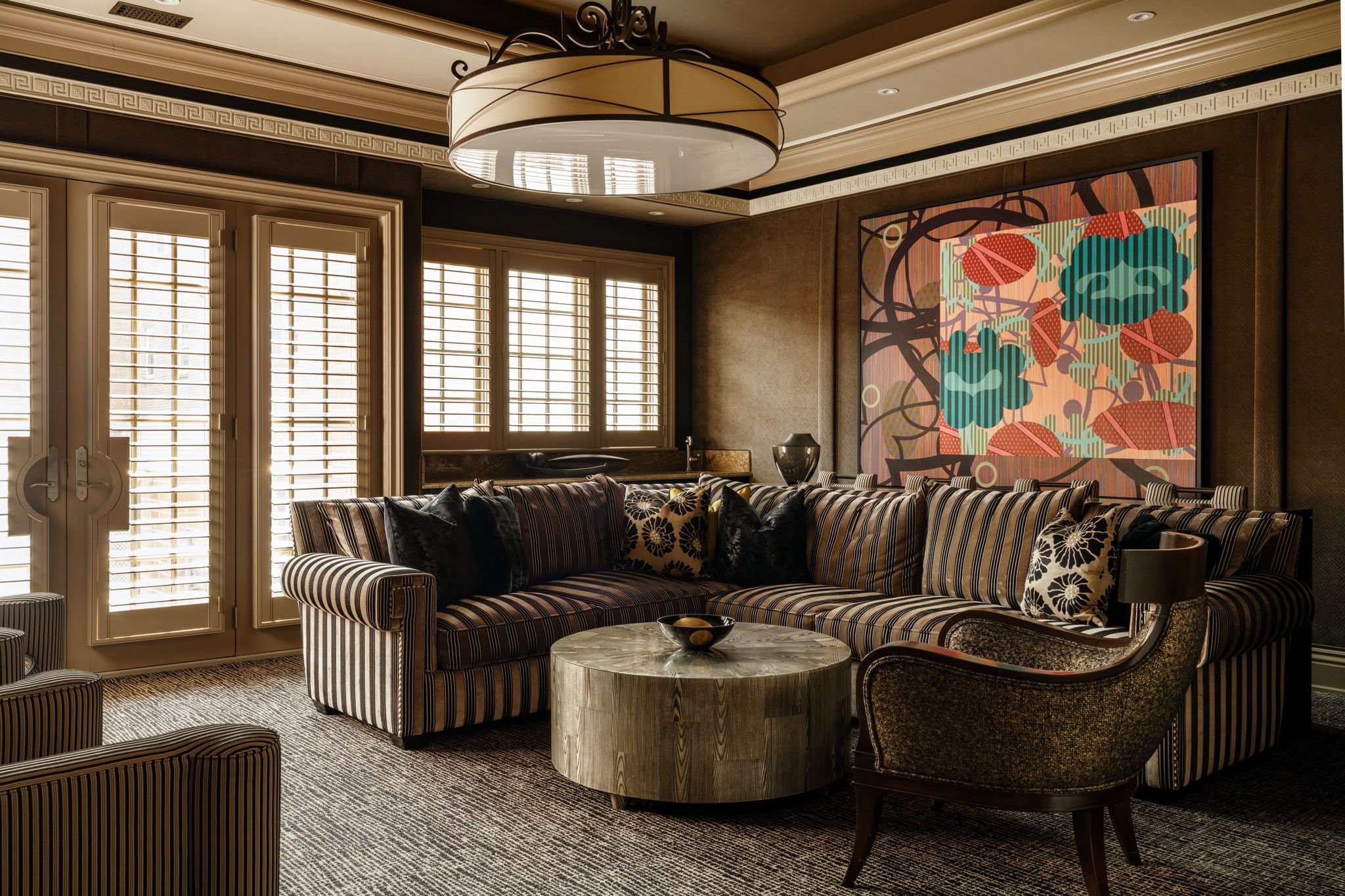 Elegant living room with striped sofa, armchair, and marble coffee table, decorated with pillows, large artwork on the wall, and wood shutters on windows.