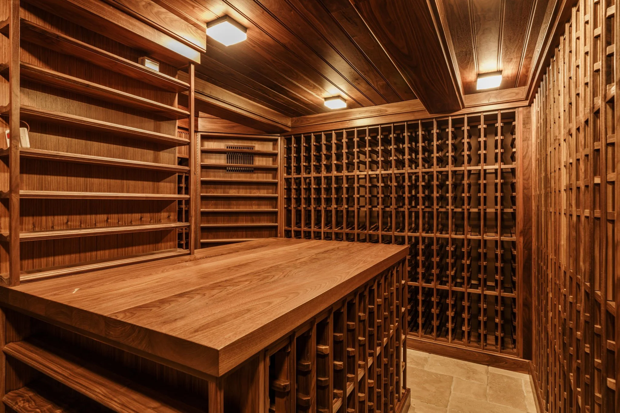 Interior view of a wood wine cellar with built-in wooden shelves and wine racks on the walls, illuminated by ceiling lights.