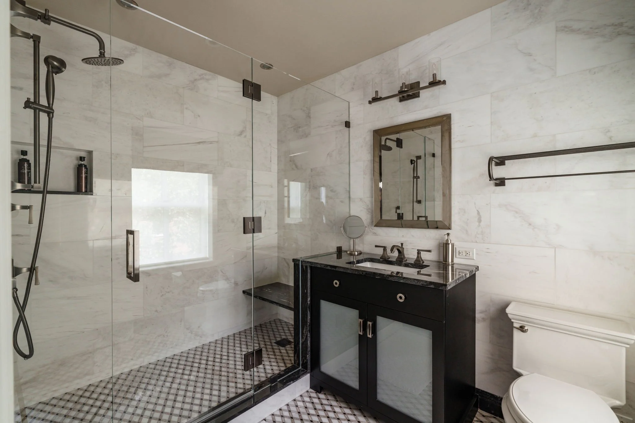 Modern bathroom with a glass shower enclosure, a black vanity with a granite countertop, and large marble wall tiles.