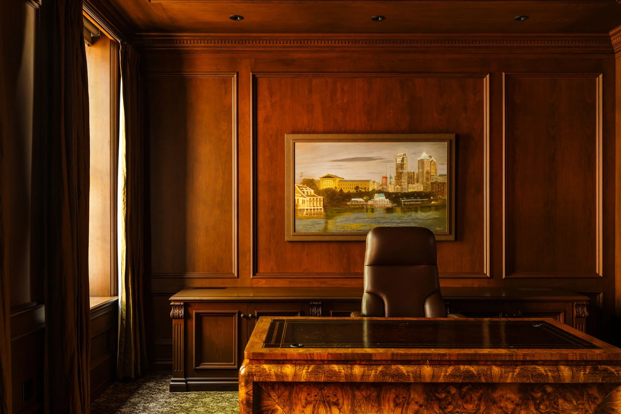 An elegant office with wood-paneled walls, a dark leather chair, and a framed cityscape painting on the wall.