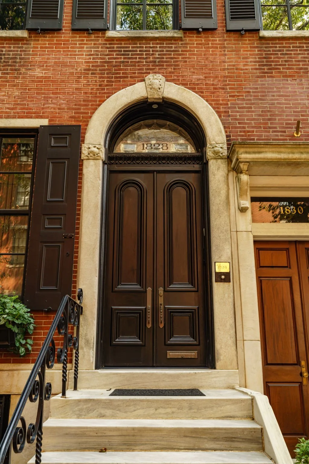 Front entrance of a historic brick building with a black arched door, stone trim, and the year 1828 engraved above the door.