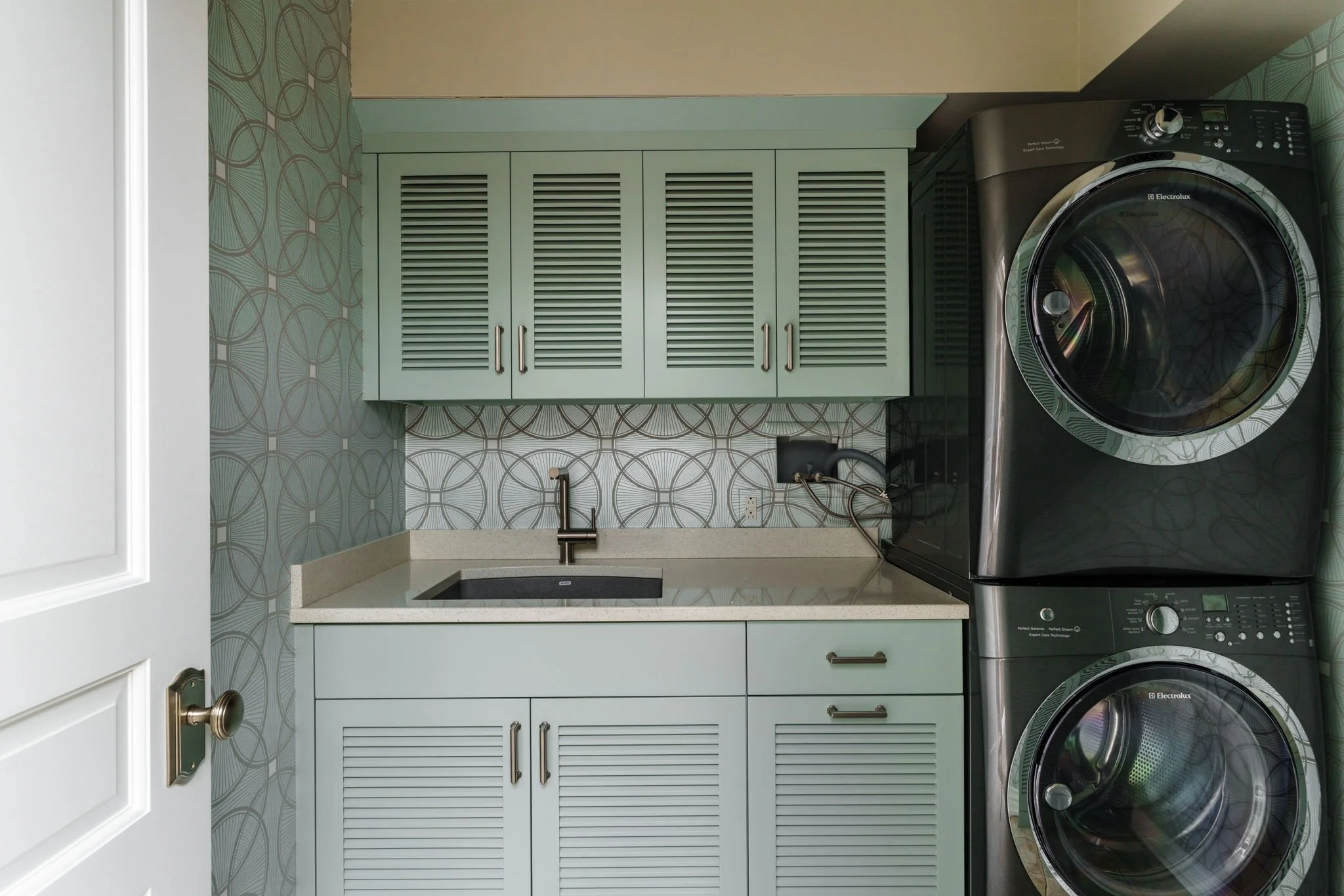 A laundry room with lime green cabinets, a patterned wallpaper, a small sink, and a black front-loading washing machine and dryer.