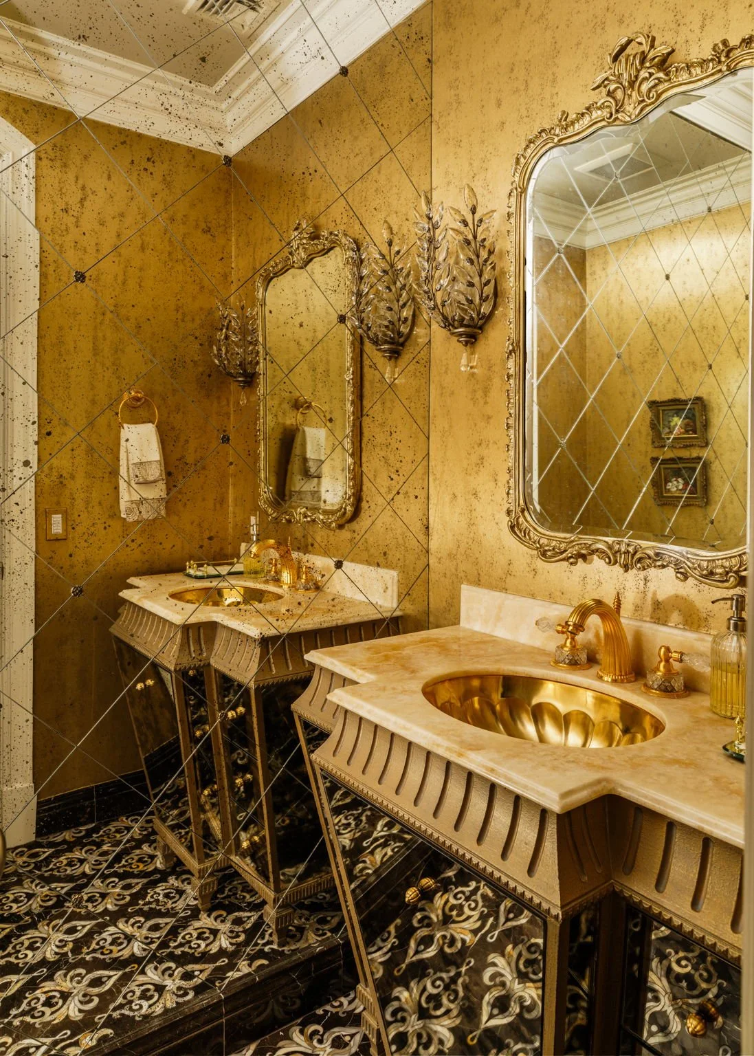 Luxurious bathroom with gold accents, ornate mirrors, and patterned black and white floor tiles.