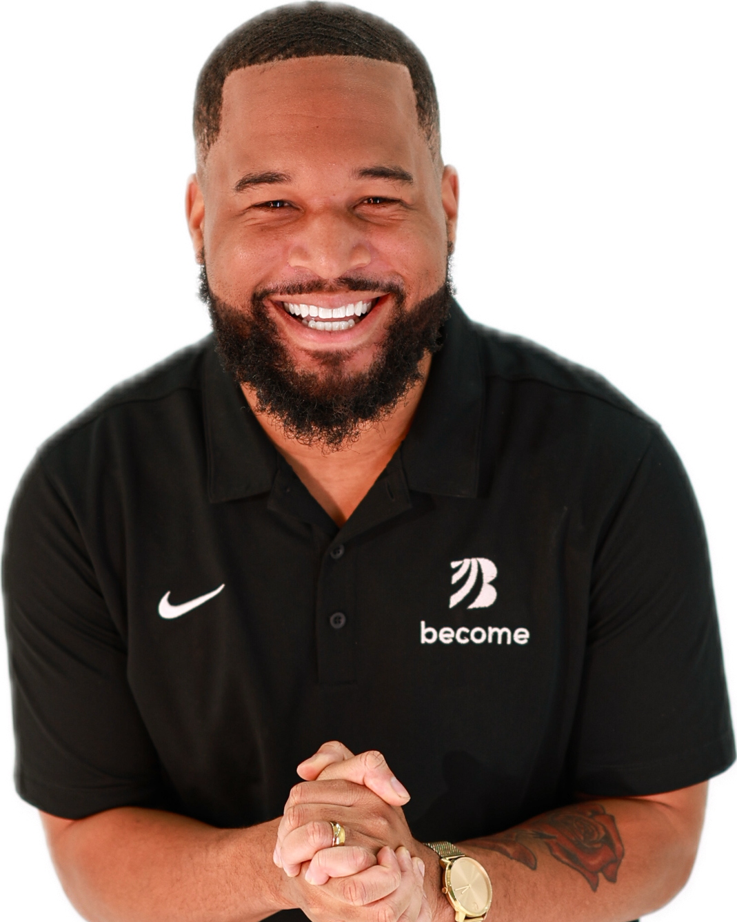 A smiling man with a beard and short hair, wearing a black polo shirt with the words 'become' and a logo on it, and a gold watch.