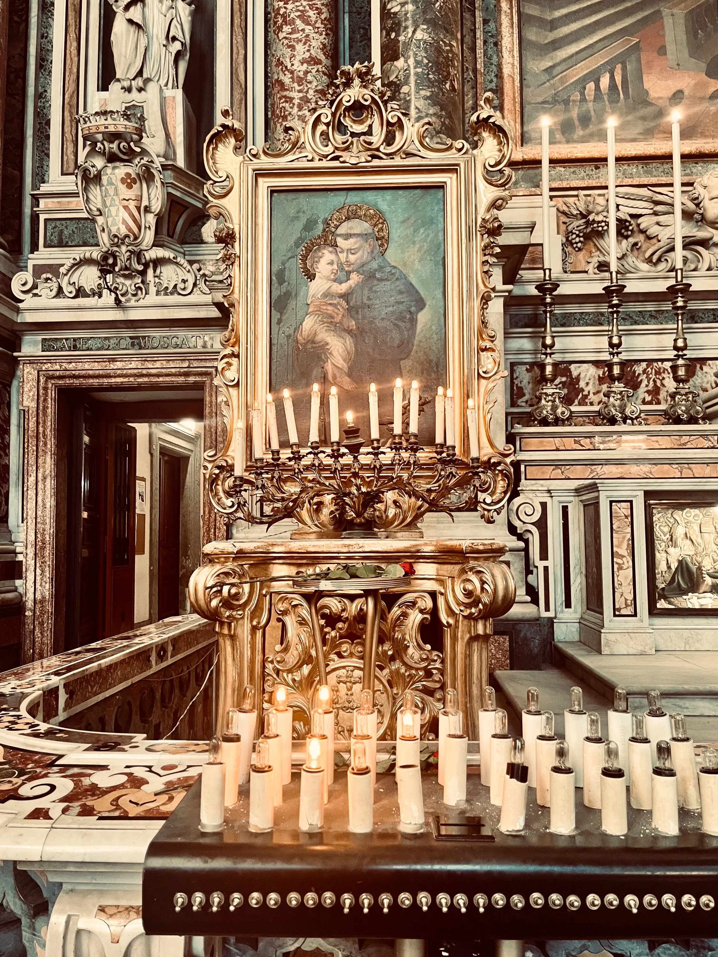 A detail from the interior of Napoli's Gesu Nuovo church. Lit candles and intricate gold embellishments, with marble and wood details in the background.