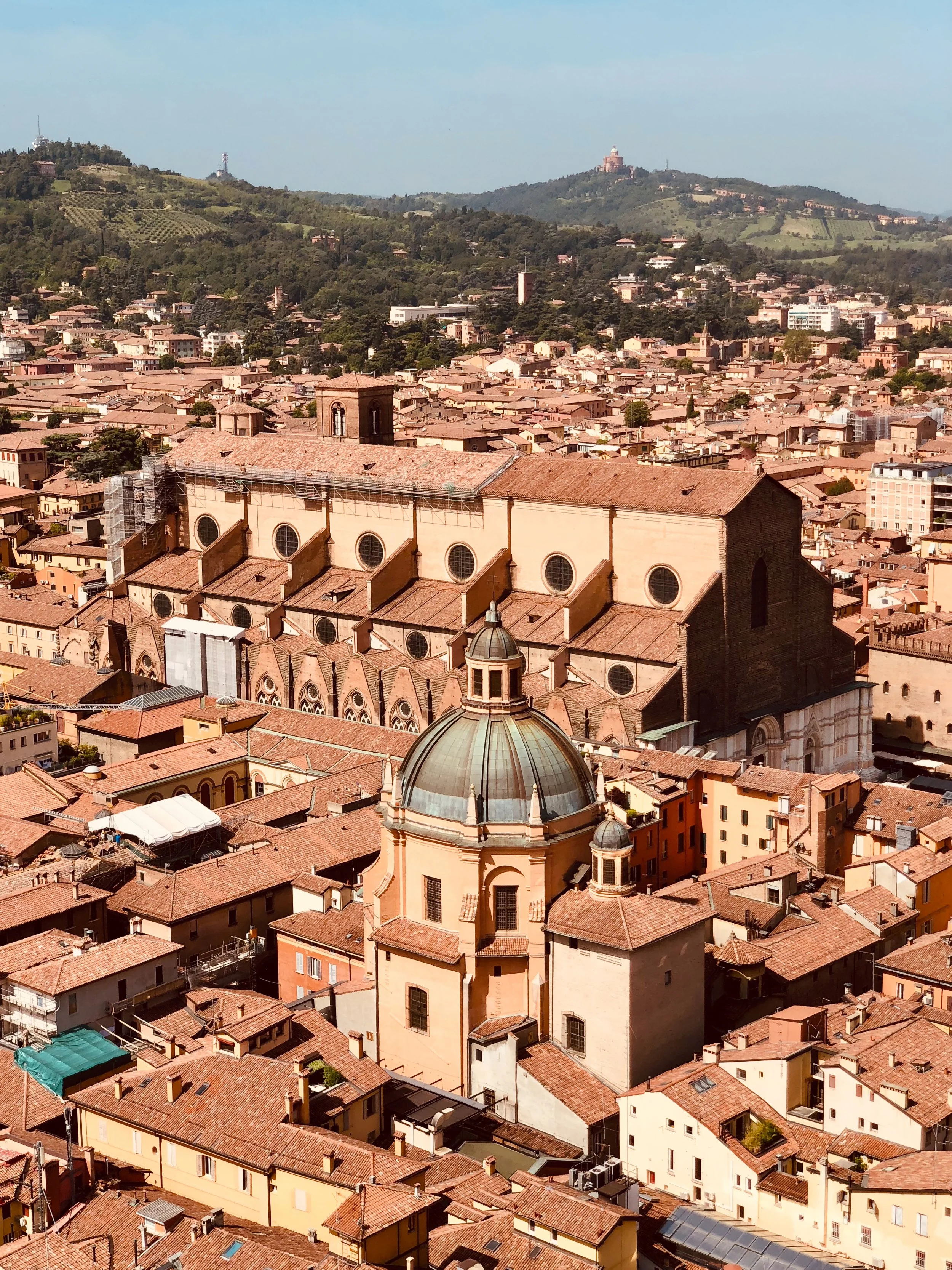 Aerial view of the city of Bologna with its red-tiled roofs, surrounded by buildings, hills, and green landscape. Come for the architecture, stay for the incredible Bolognese food.