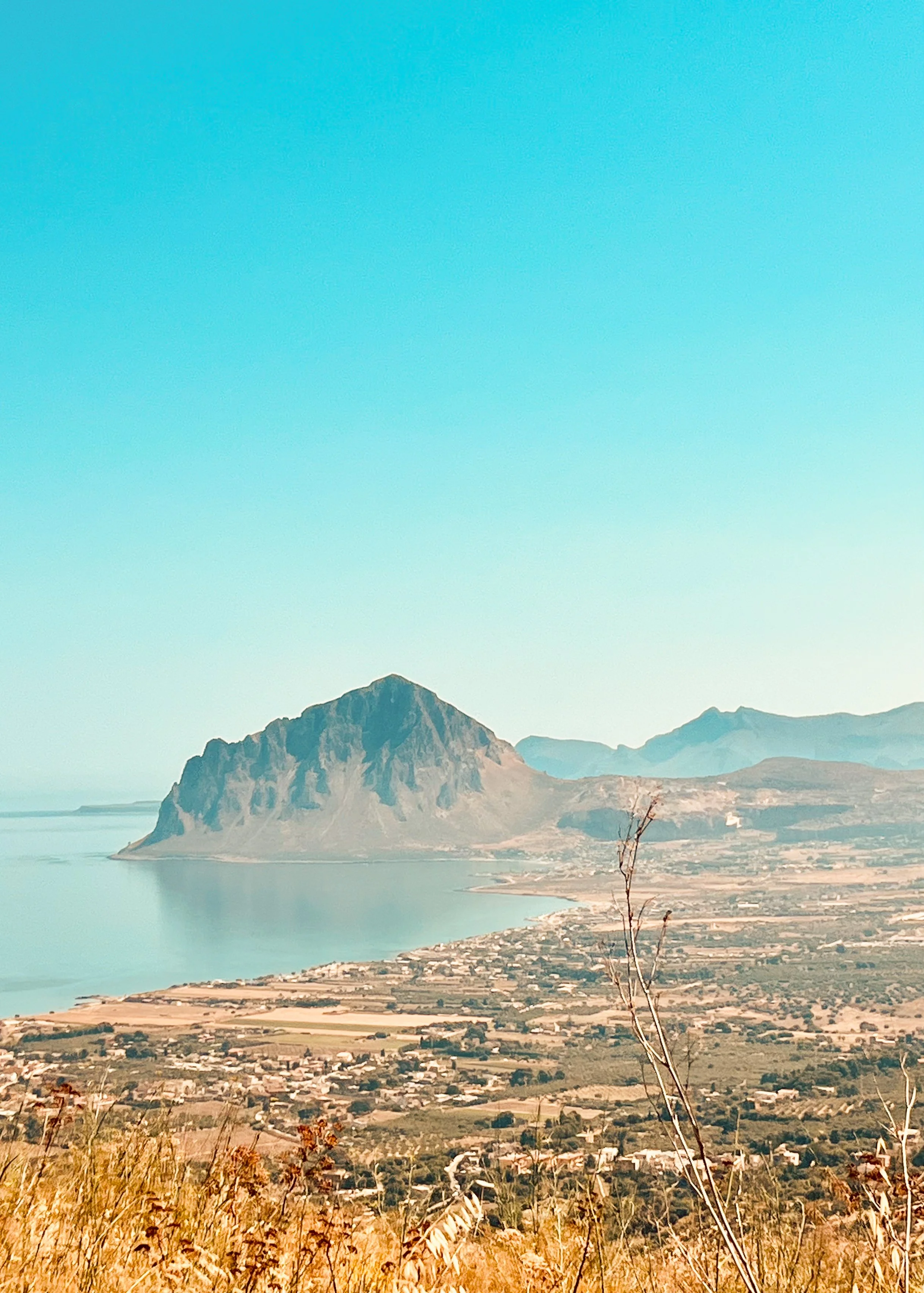 A sweeping Sicilian view from the village of Erice with Monte Cofano seen in the distance. The Mediterranean Sea hugs the shore.