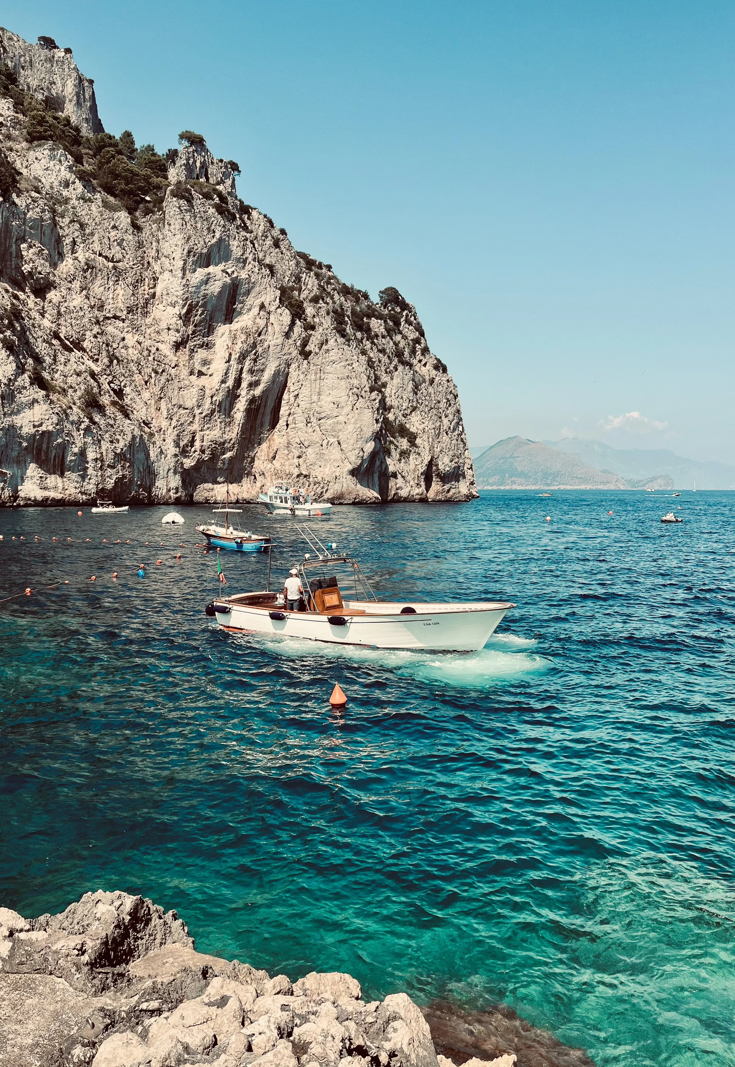 A wooden boats anchored near rocky coastline of Capri, Italy.
