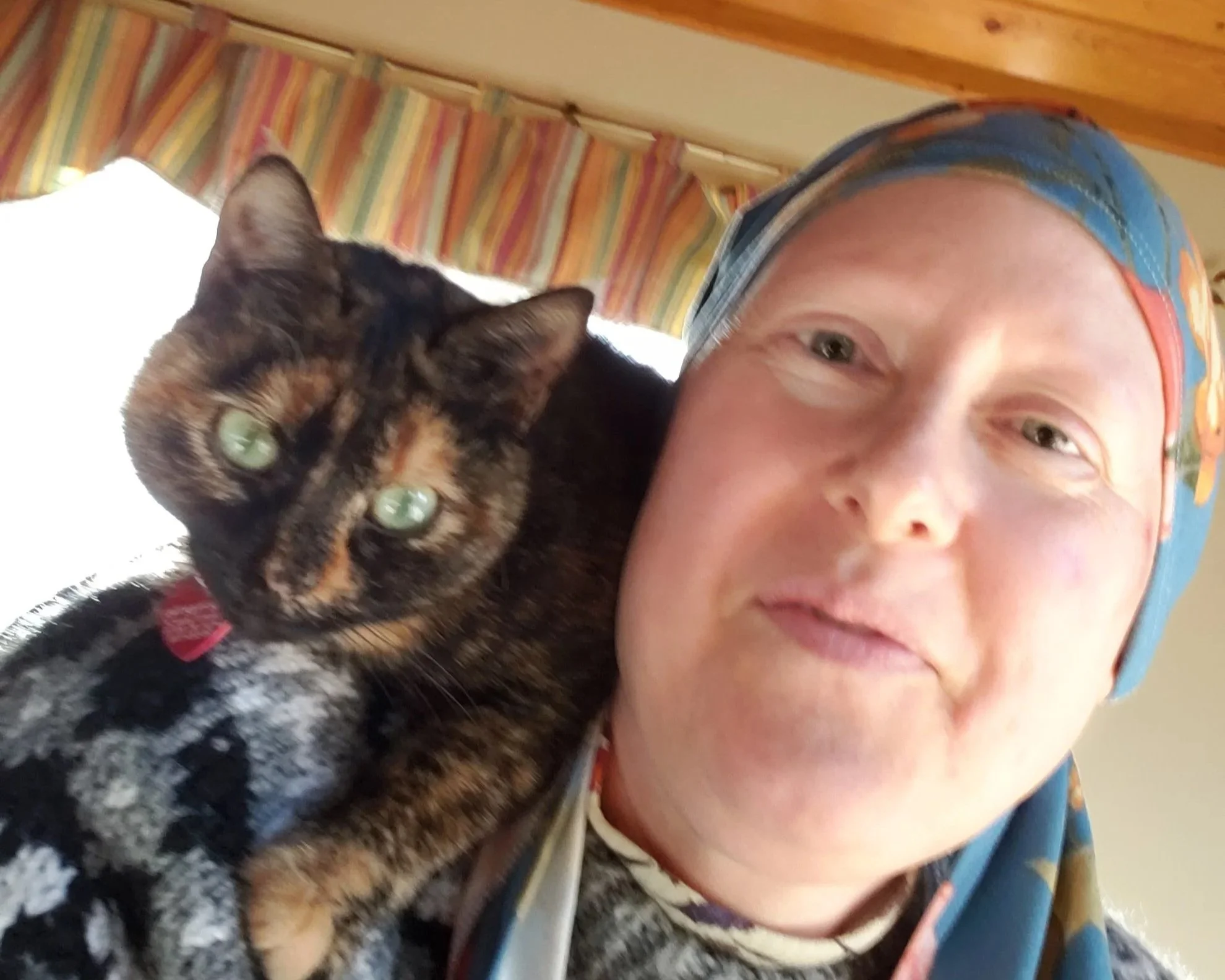 Amy in February 2023 wearing a colorful headscarf holding Sunrise Hope, her green-eyed tortoiseshell cat.
