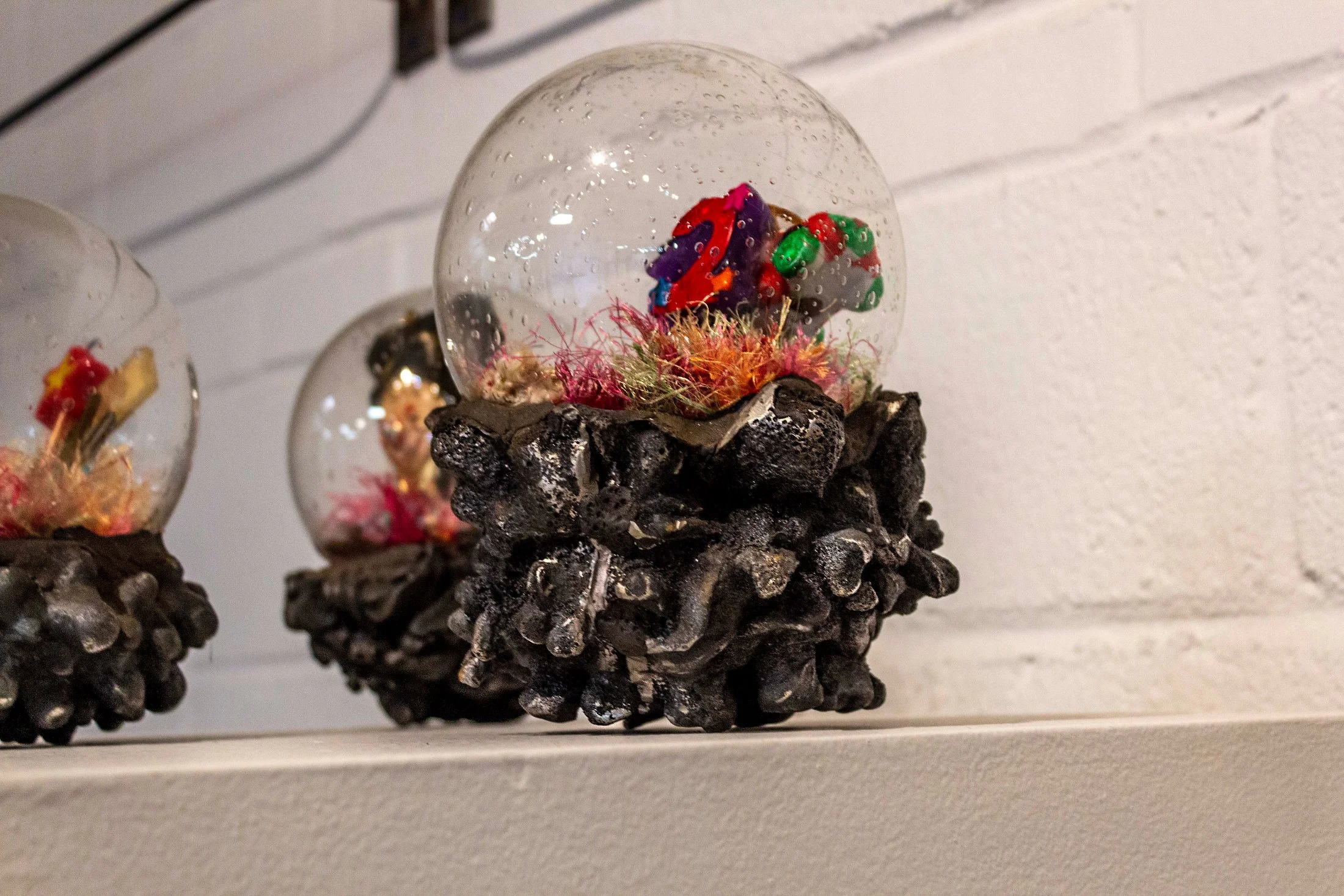 Glass snow globe with colorful sprinkles and red, purple, and green decorations inside, resting on a textured black base.