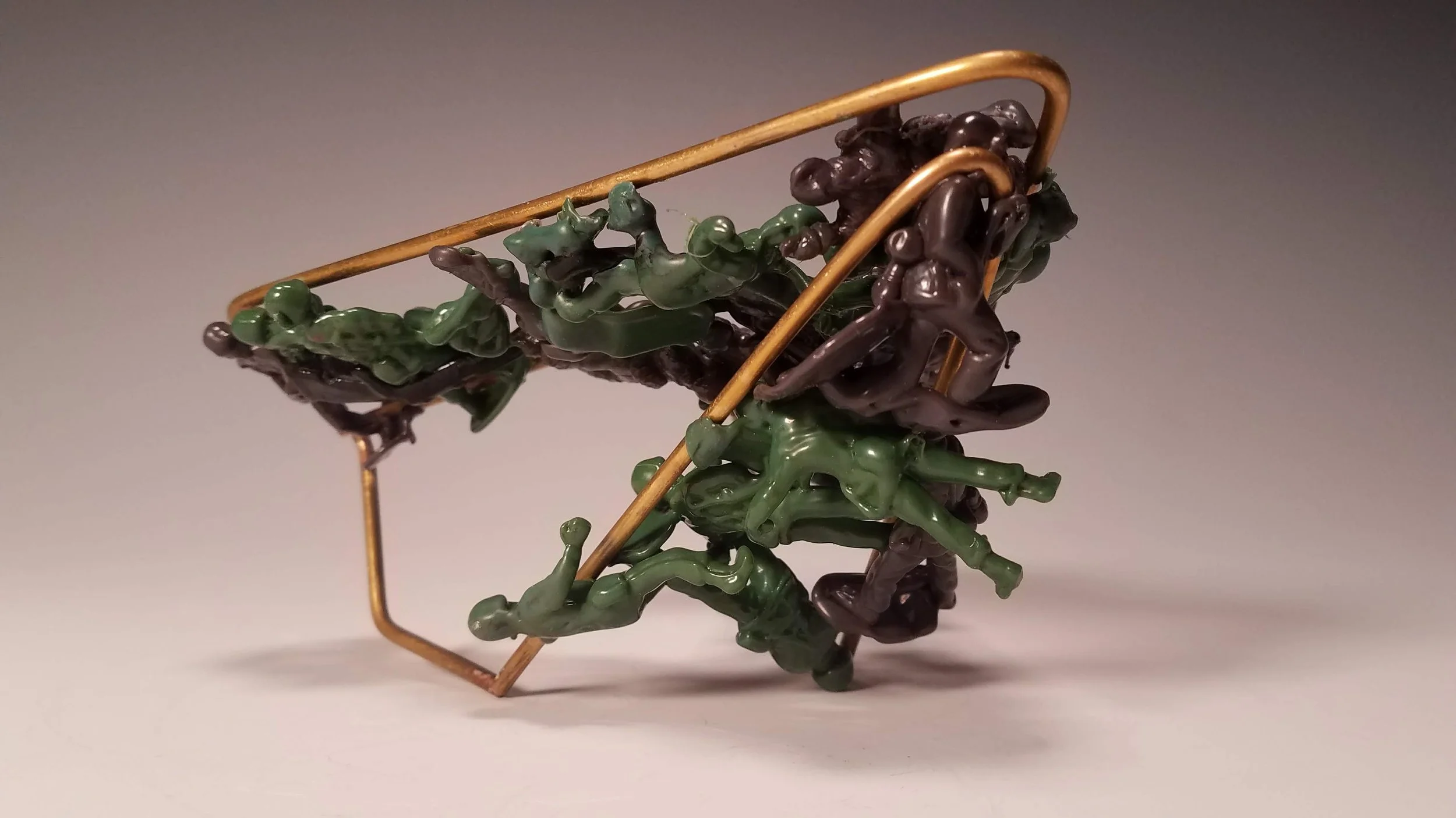 Sculpture of intertwined green and dark brown toy soldiers melted and supported by a gold wireframe. 
