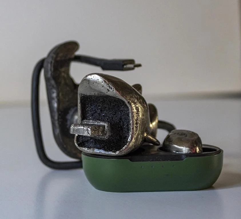 Close-up of a cast iron decorative shark designed for a charging block. From the shark's square shaped month a plug emerges, resting on a green ear bud container.