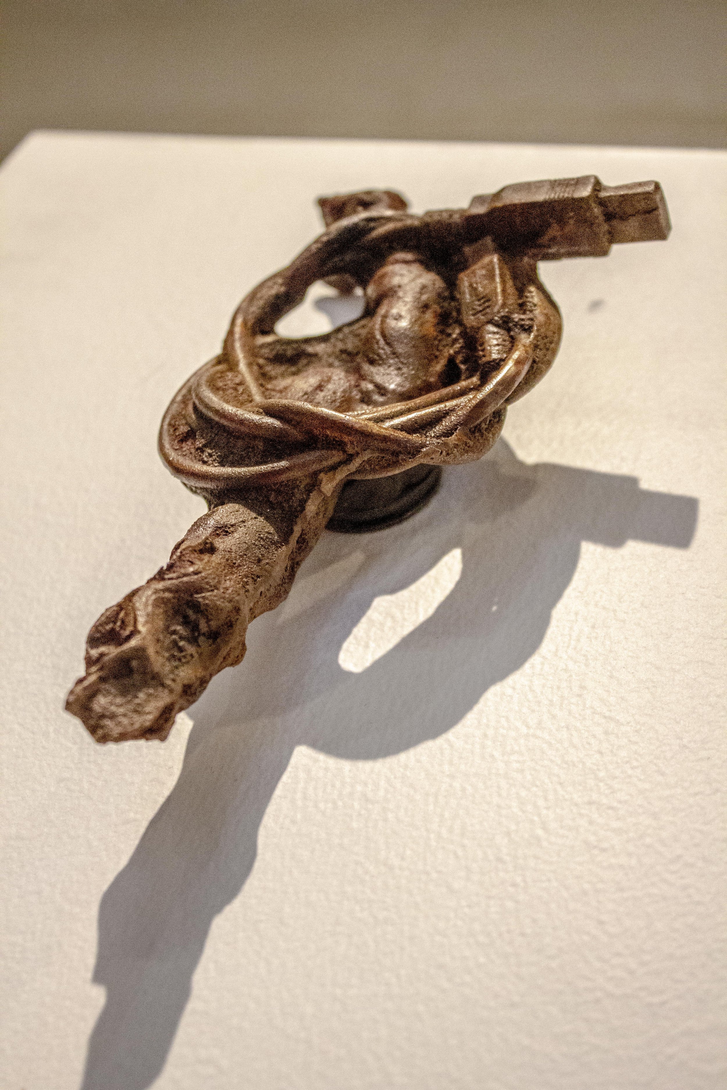 A detailed cast iron sculpture of a root wrapped in an electronic charging cord, displayed on a white surface with a shadow cast on the background.