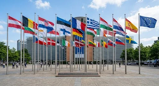 Multiple European and international flags flying in front of a government or institutional building.