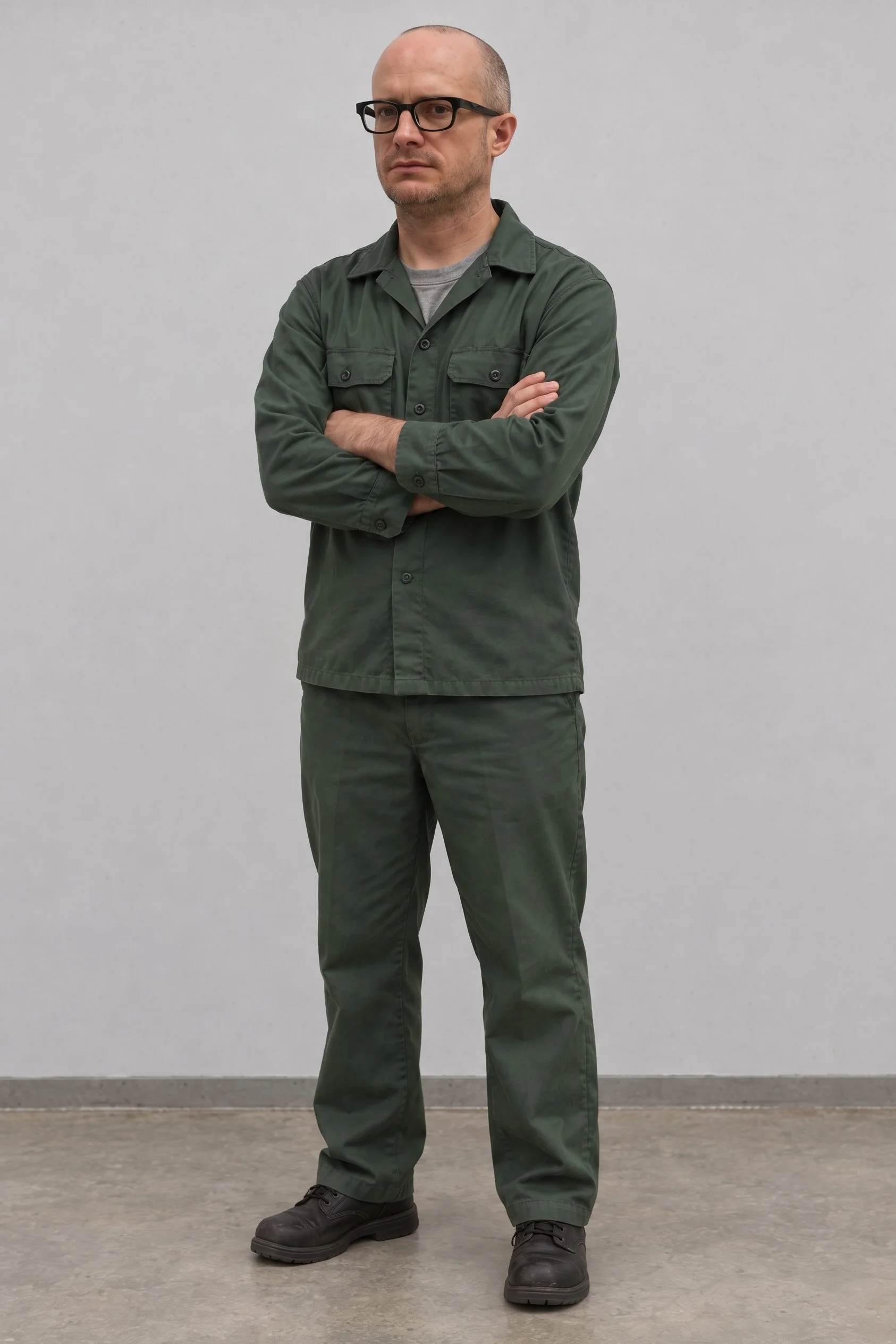 Mike Collins standing with arm crossed in a green minimum security federal prison camp uniform