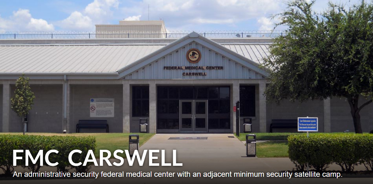 Front view of FMC Carswell, a federal medical center with a white metal roof, surrounded by greenery and benches, with signage indicating it's a federal medical center in Carswell.