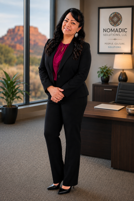 Professional woman standing in an office with a window view of a rocky landscape, near a desk with a lamp, plants, and a framed company logo.