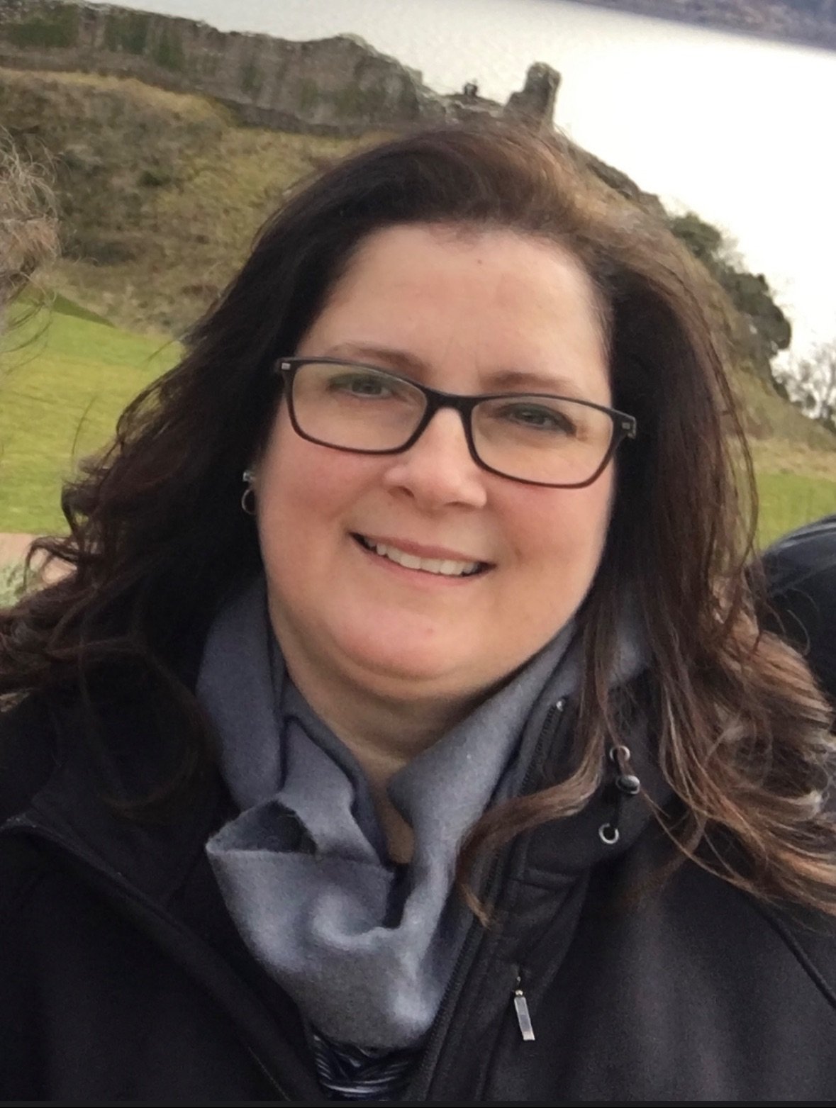 Caroline Ray, contemporary romance author, smiling outdoors near a hillside castle ruin.