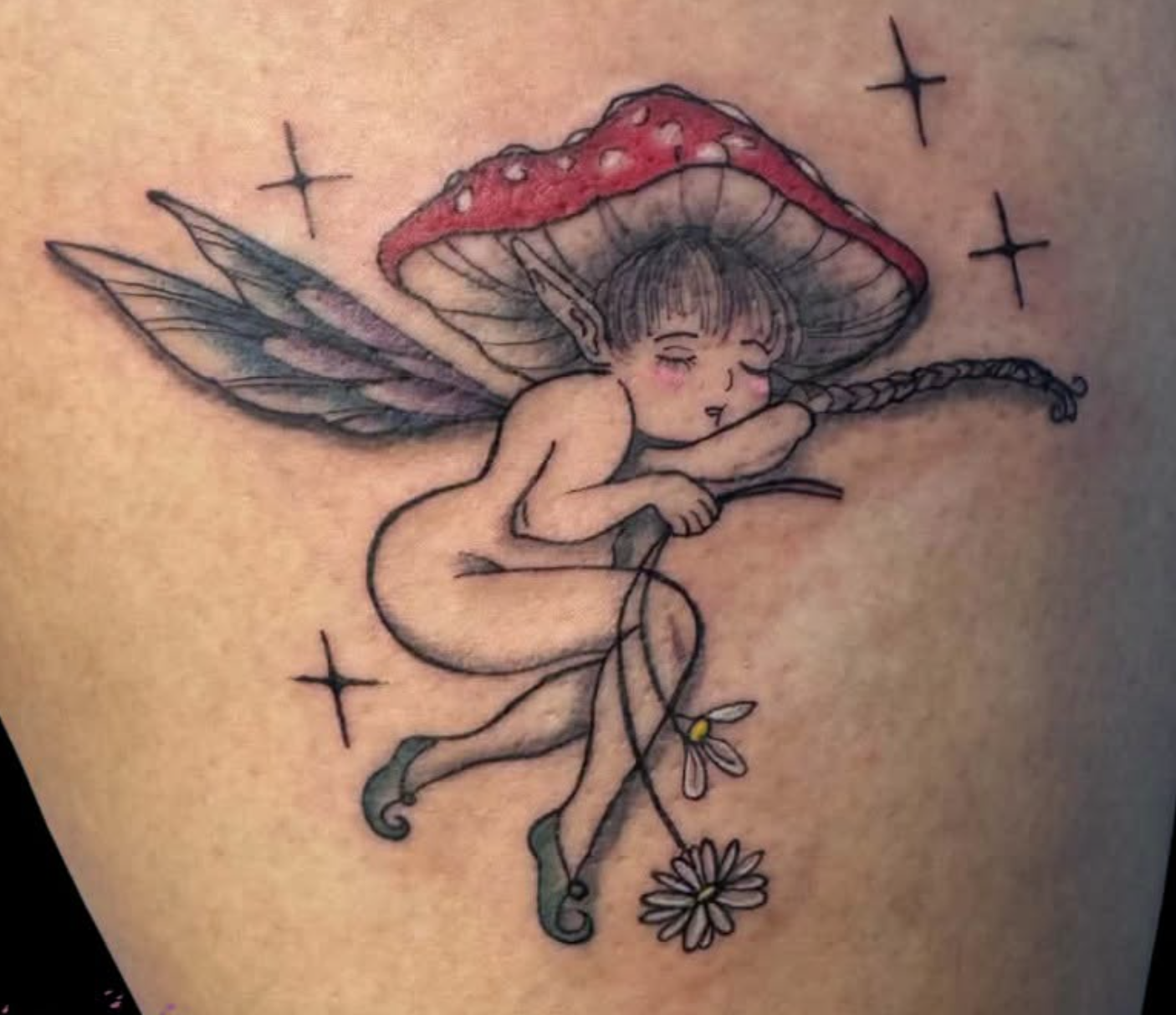 A tattoo of a fairy with large wings, holding a flower, with a mushroom cap as a hat, and stars around her, on skin.