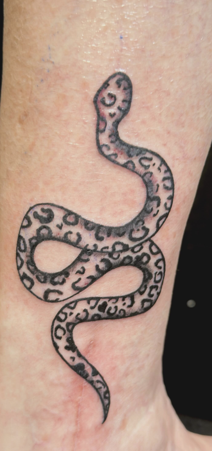 Tattoo of a snake with a leopard print pattern on skin.
