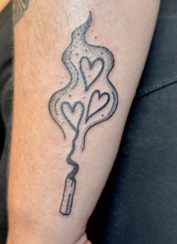 Tattoo of a lit cigarette with smoke forming three hearts.