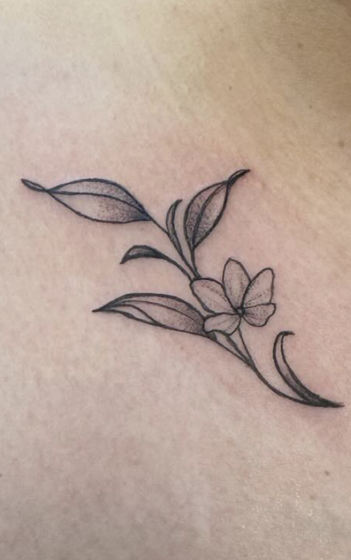 Black and gray outline tattoo of a small flower with five petals and leaves on a person's skin.