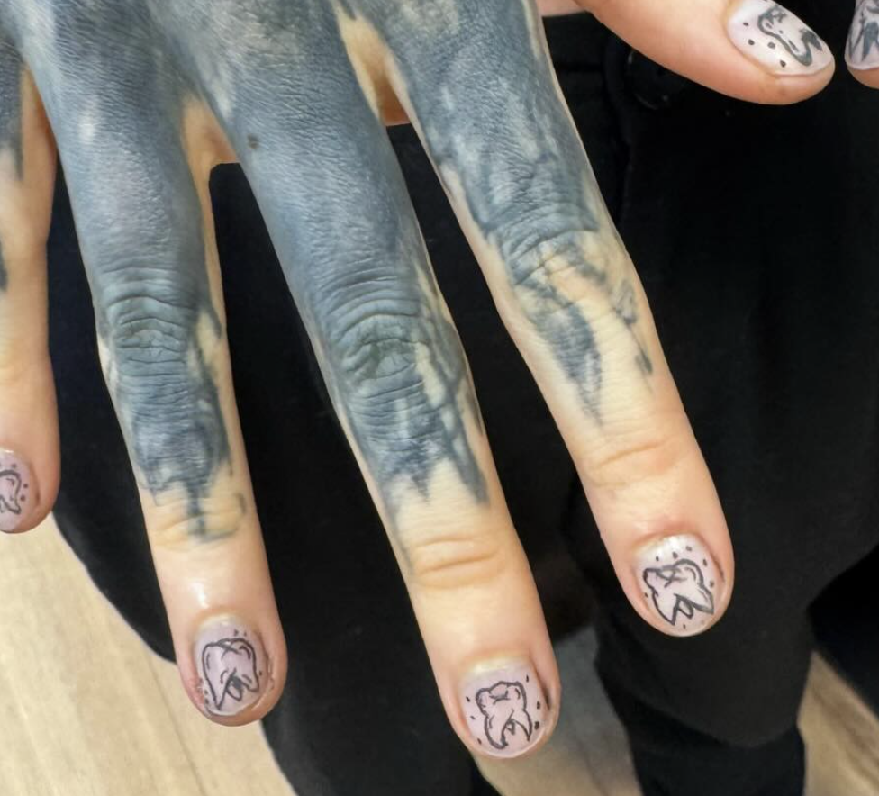 A person's hand covered in intricate black and gray tattoos of animals on the fingers, with small, simple line drawings of chickens on their nails.