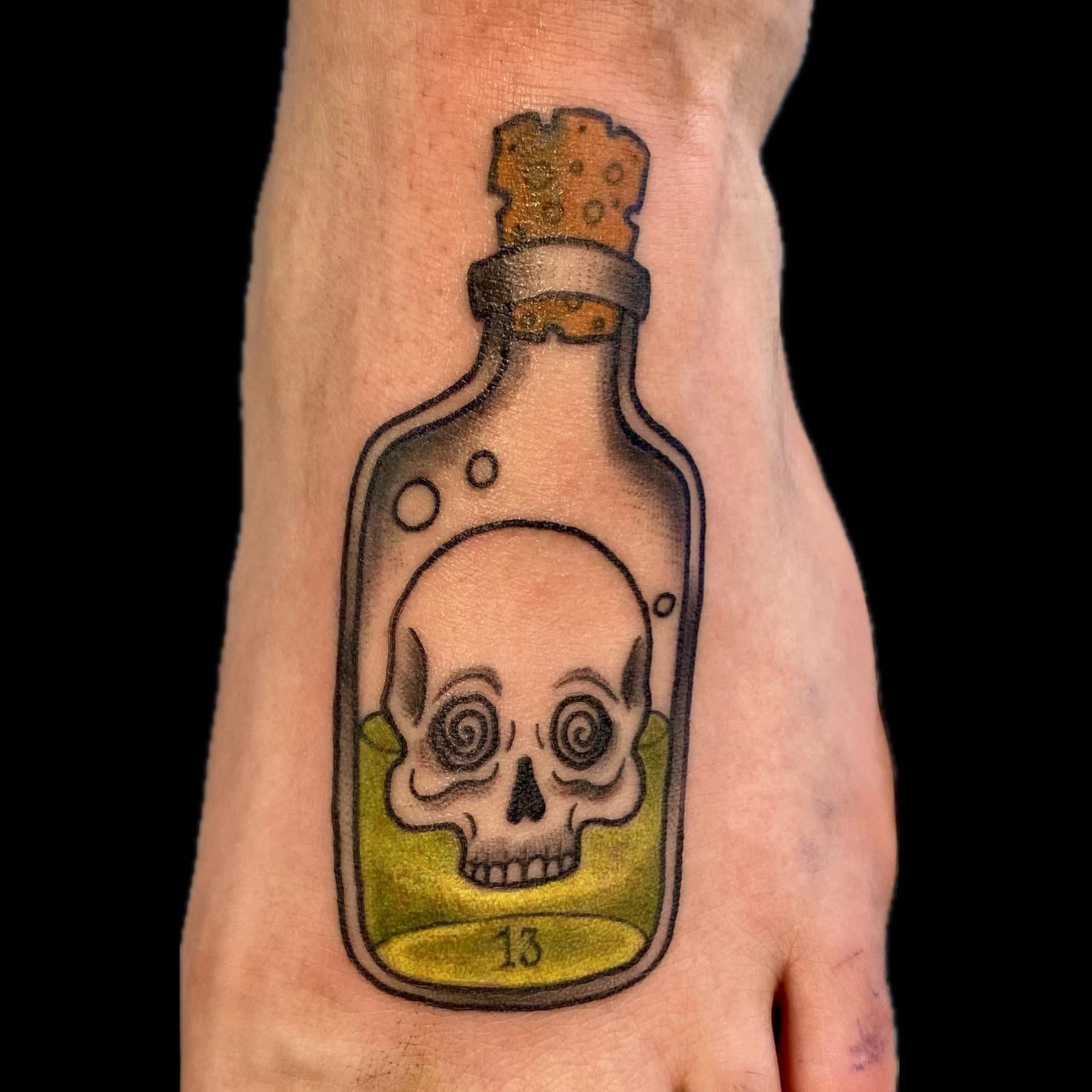 Tattoo of a colorful cartoon-style skull inside a bottle, with a yellow background and black outlines.