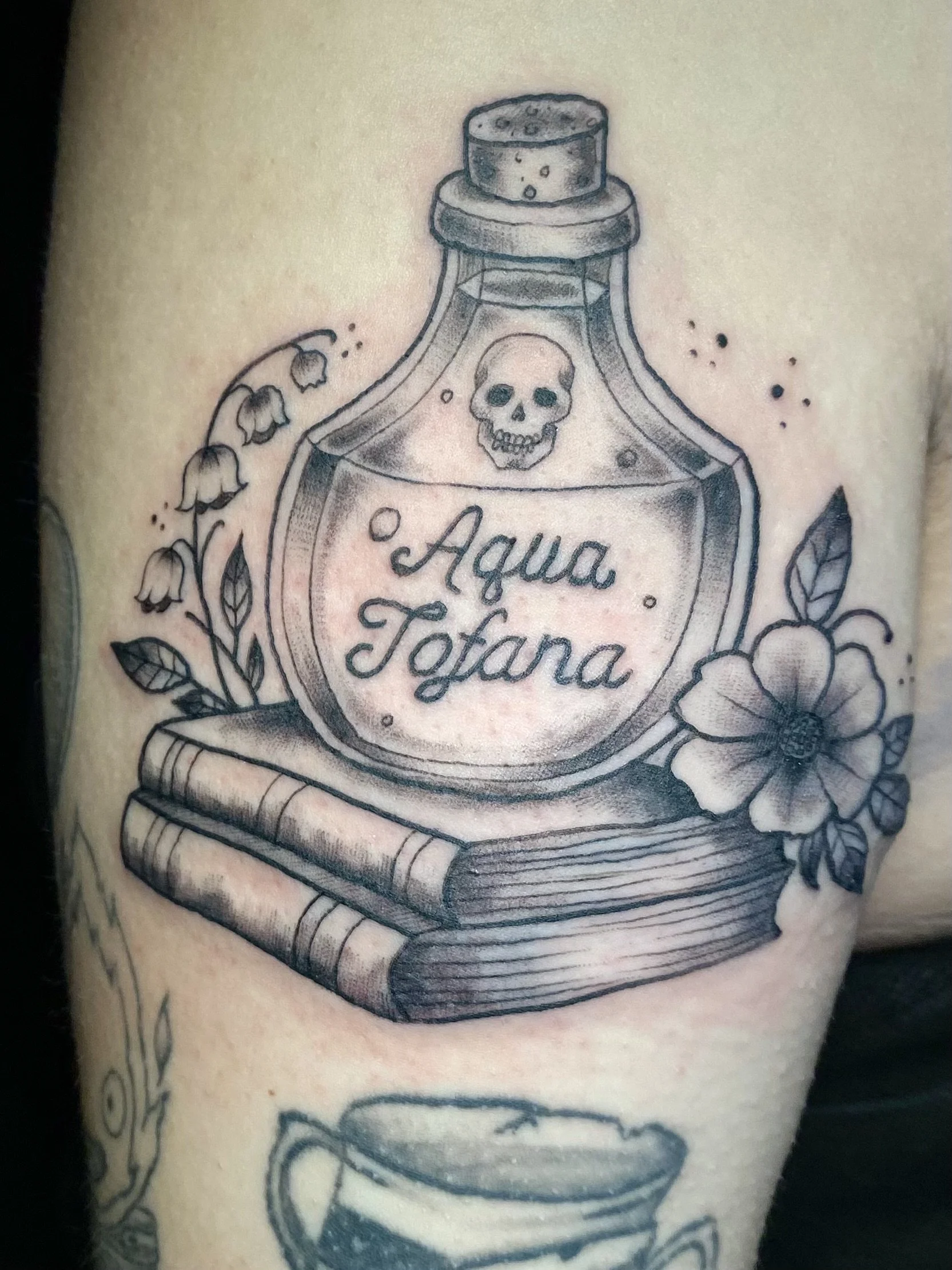 Tattoo of a medicine bottle labeled "Aqua Totana" with a skull and flowers surrounding it.