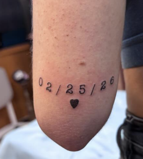 Tattoo on the elbow displaying the date 02/25/26 with a small heart below.