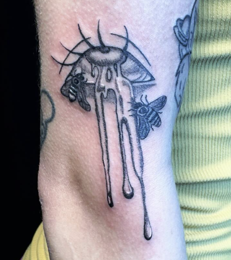 Tattoo of a bee and a moth with dripping ink or paint on upper arm.