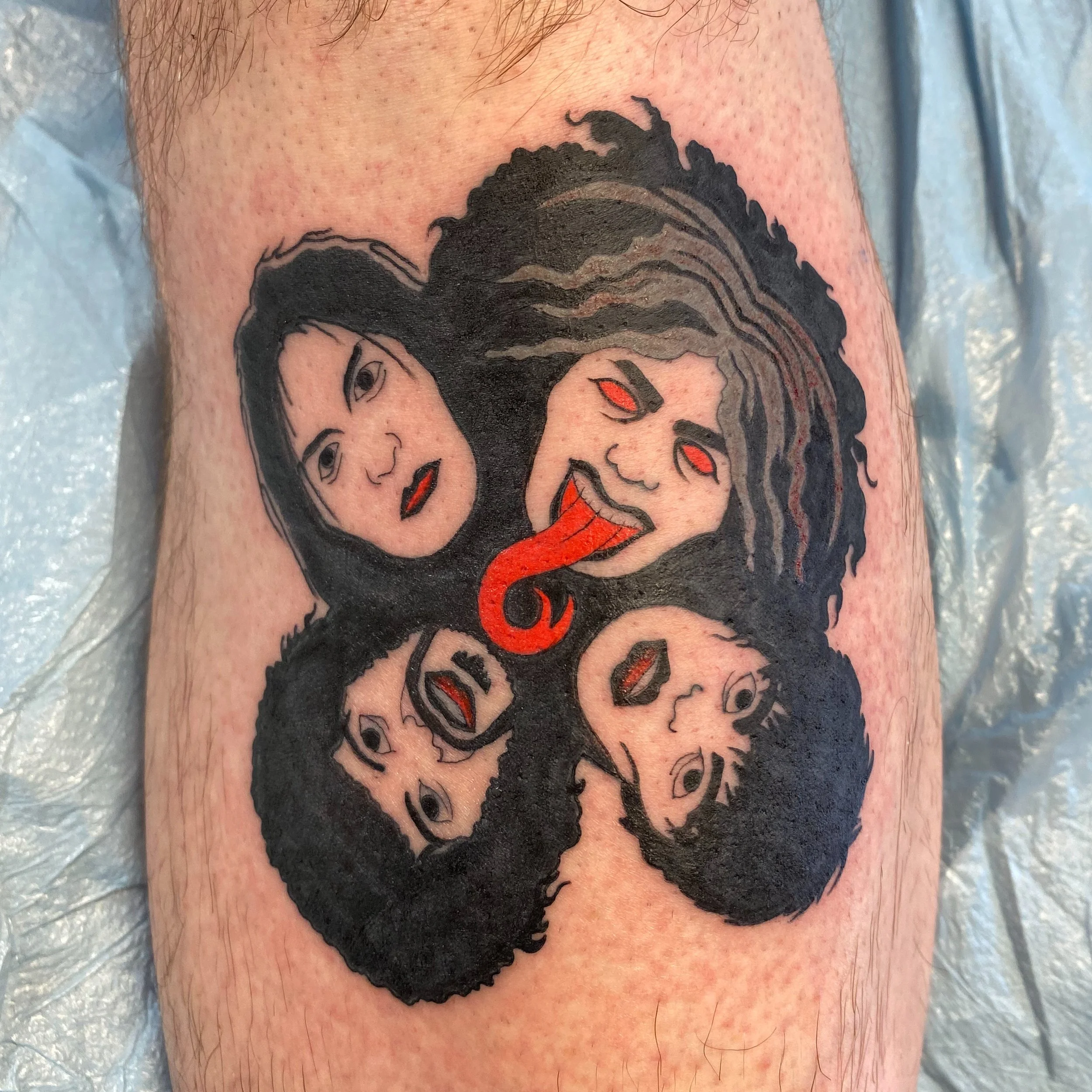 Tattoo of a man's face with red eyes and black swirling hair on a person's arm.