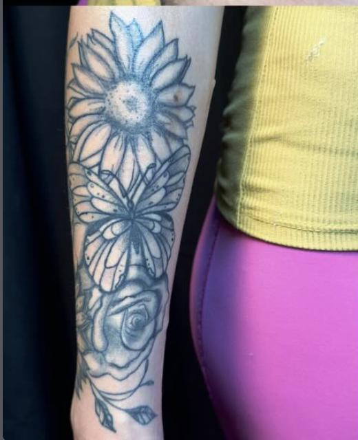 Tattoo of a sunflower, butterfly, and a rose on a person’s forearm.