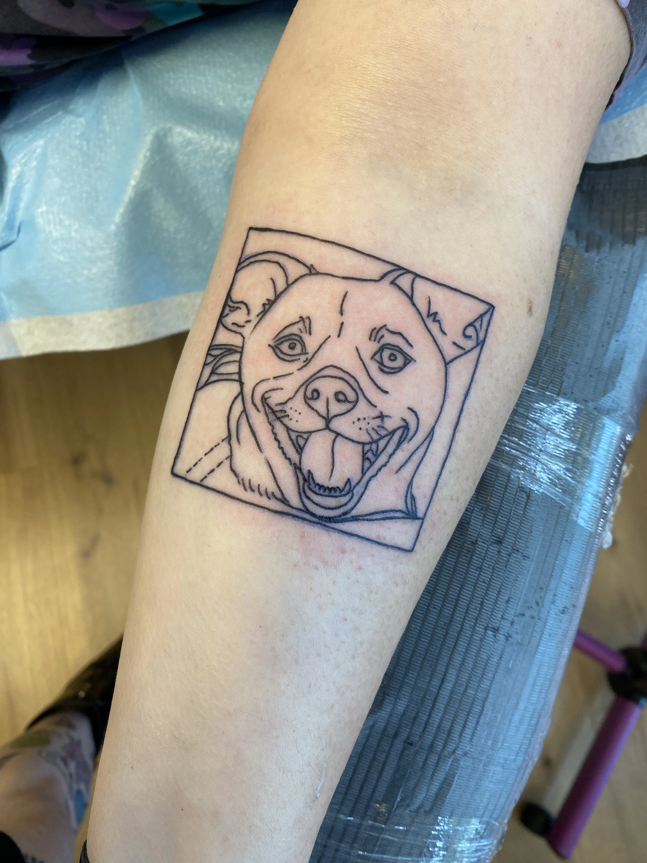 Tattoo of a dog's face in a geometric style on a person's arm.