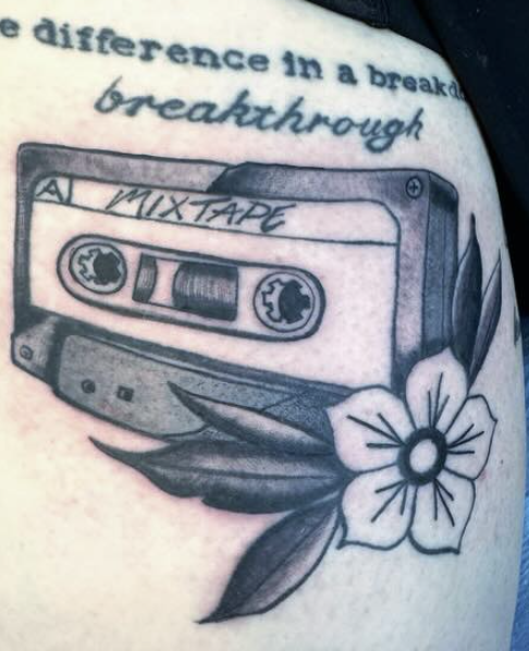 Tattoo of a cassette tape labeled 'Mixtape', with a flower and leaves, and part of a quote above it.