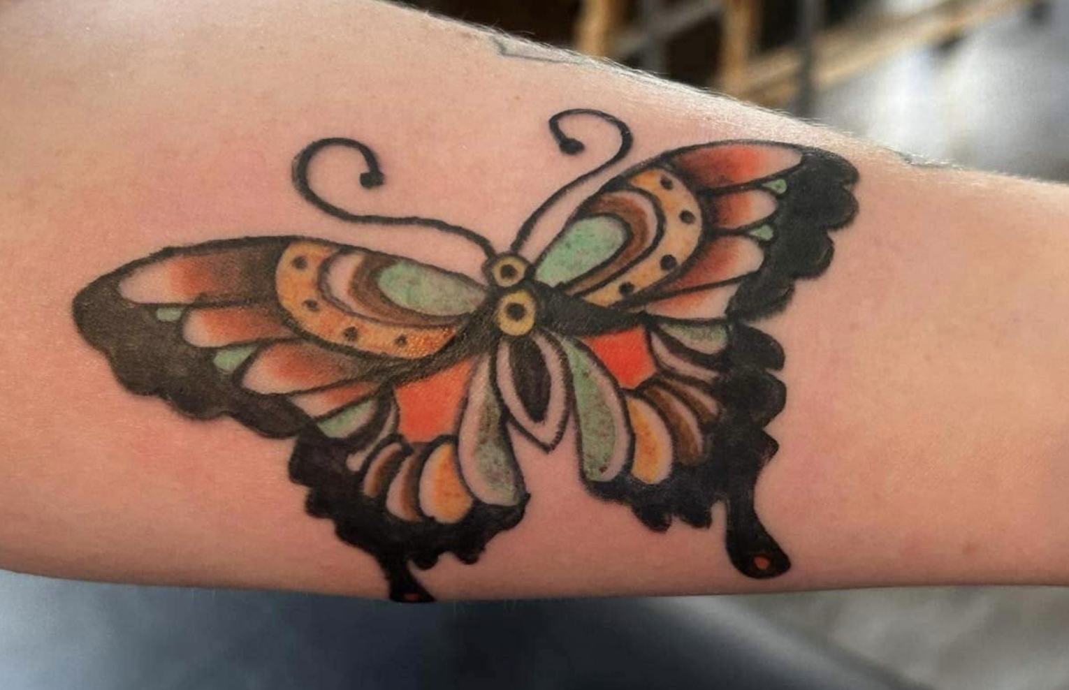 Colorful butterfly tattoo with orange, green, black, and yellow details on a person's skin.