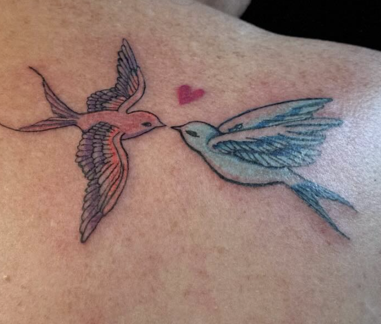 A tattoo of two hummingbirds facing each other with a small red heart above them.