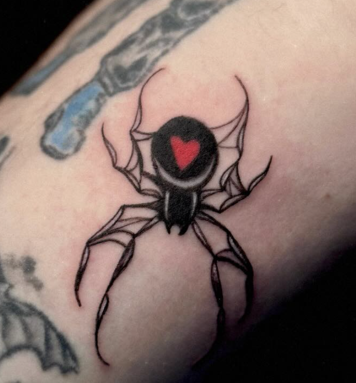 Tattoo of a black spider with a red heart in the center of its body on skin.
