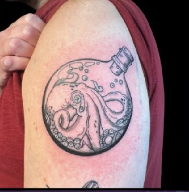 Tattoo of an octopus inside a glass bottle on the upper arm.