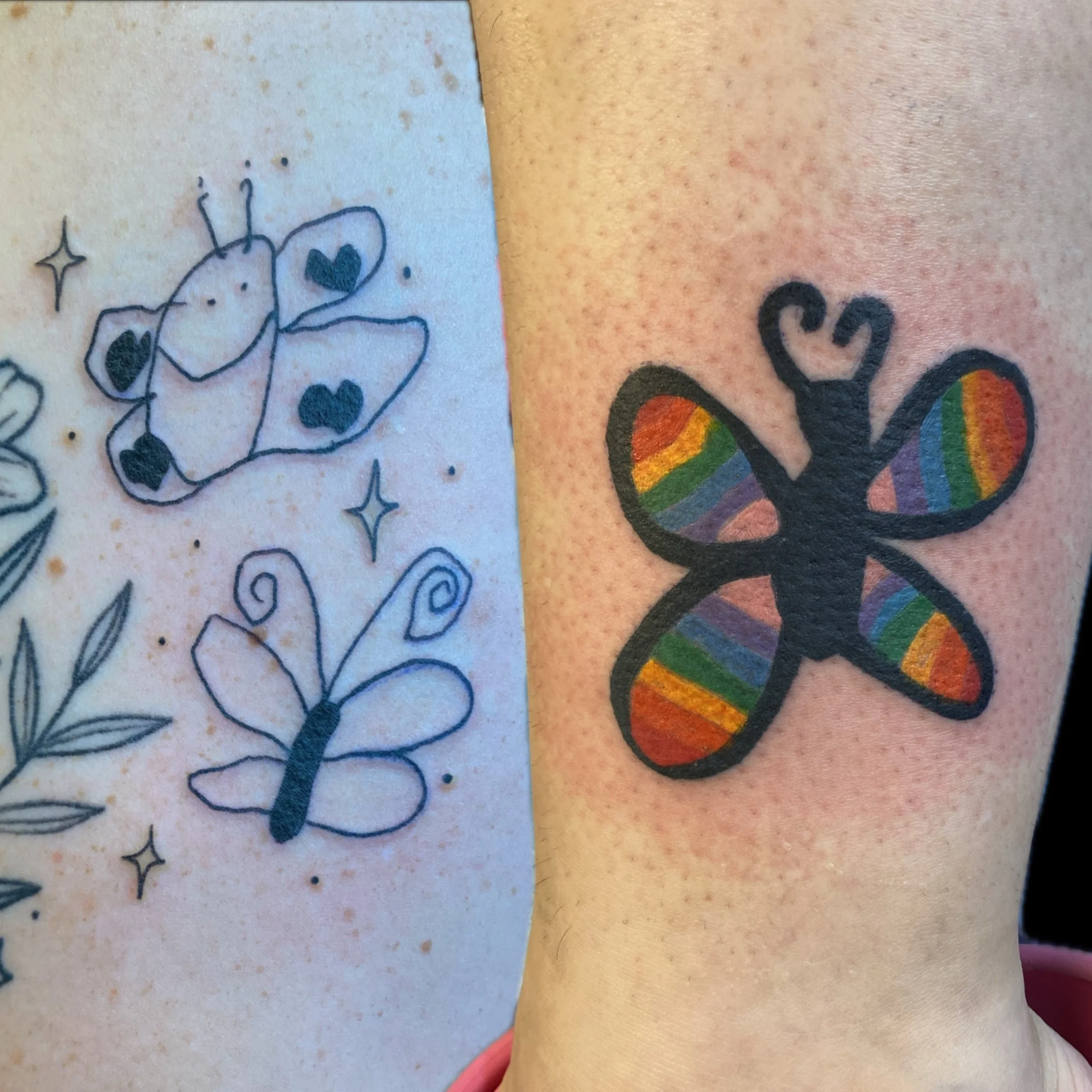 Part of a person's skin with two tattoos; one tattoo on the left depicts a flower with hearts in the petals, and the other on the right shows a rainbow-colored butterfly.