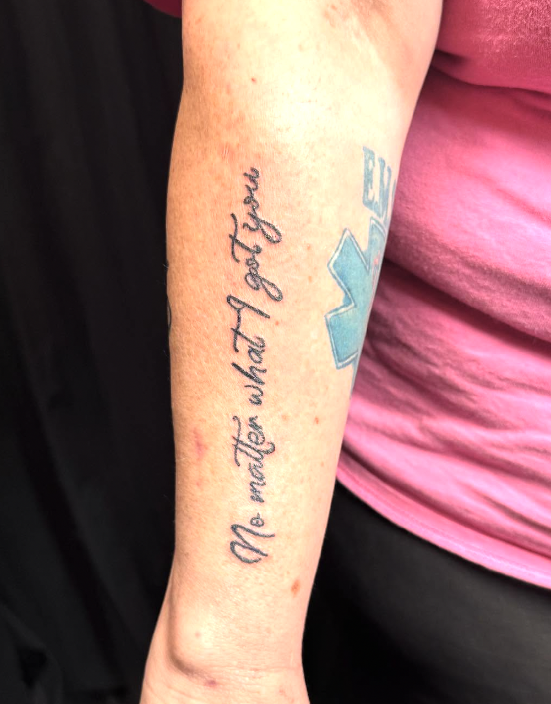 A tattoo on a person's forearm with the text 'He made what I hope you' and a blue cross symbol.