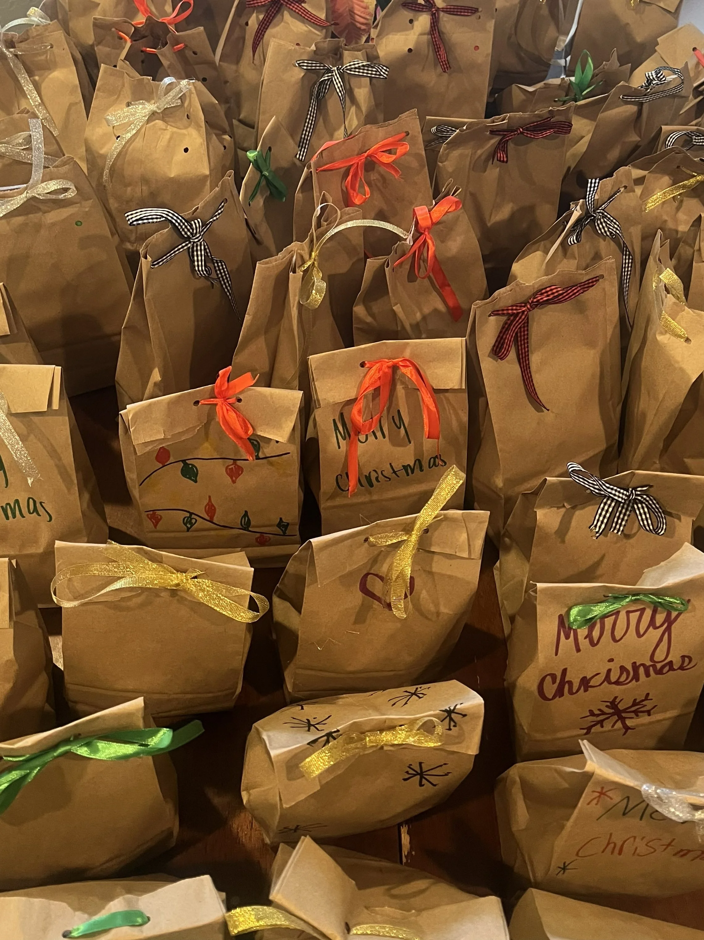 Several brown paper gift bags decorated with colorful ribbons and handwritten messages celebrating Christmas.