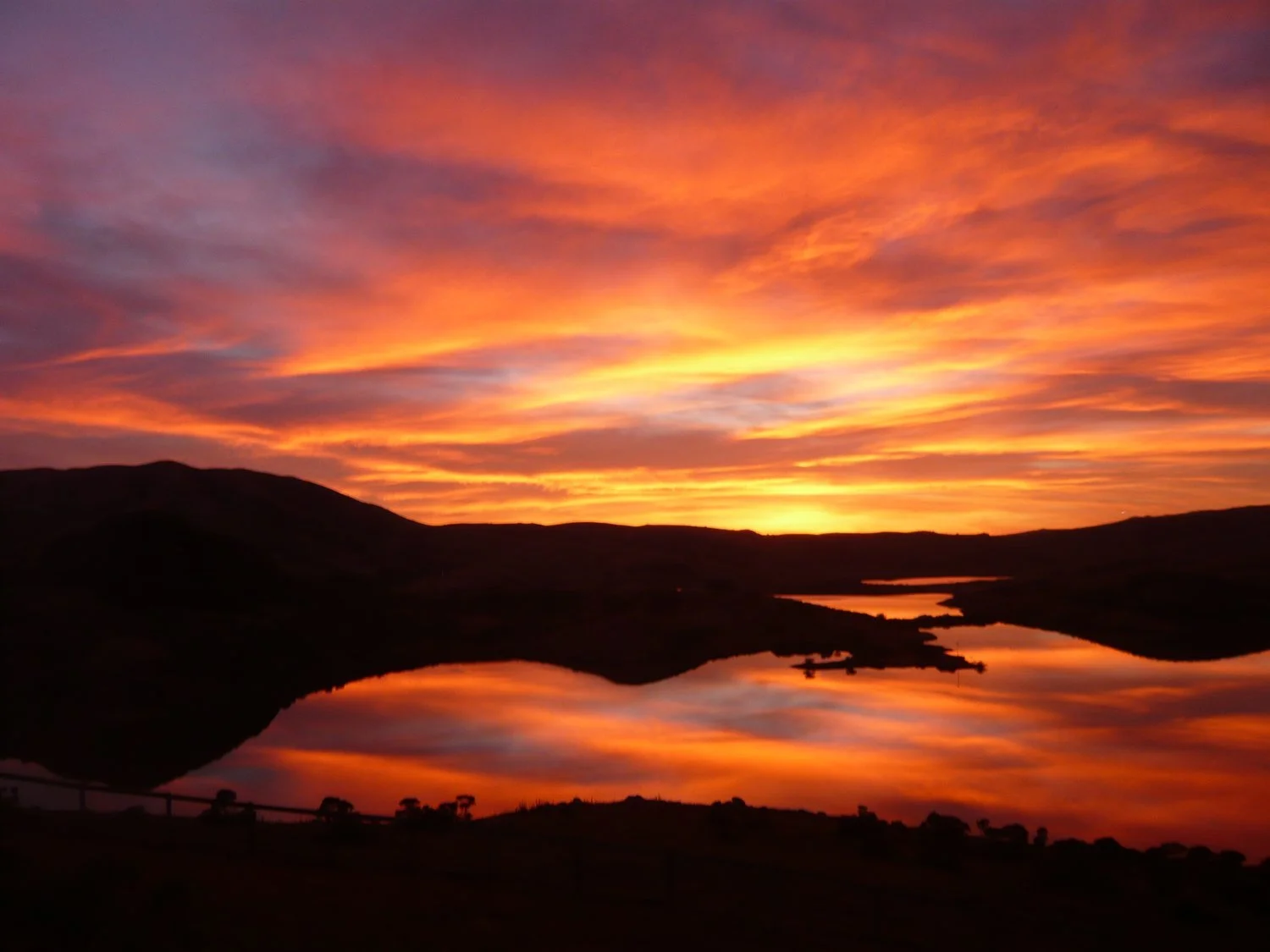 Sunset over a lake with colorful sky and silhouetted hills.