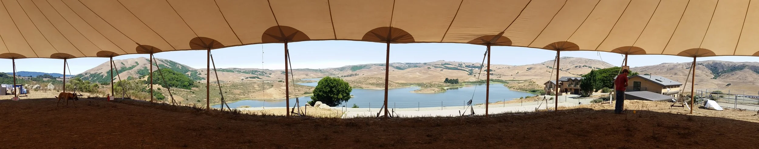 A person is on a construction site under a large canopy with a view of a lake and hills in the background.